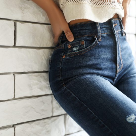 Woman wearing jeans near brick wall indoors, closeup
